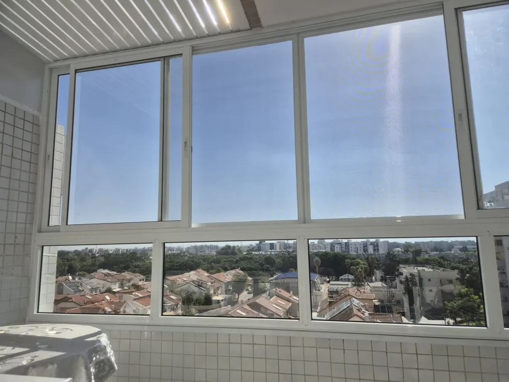 סגירת מרפסת בחלונות אלומיניום לבנים מעל קיר חיפוי אריחים
