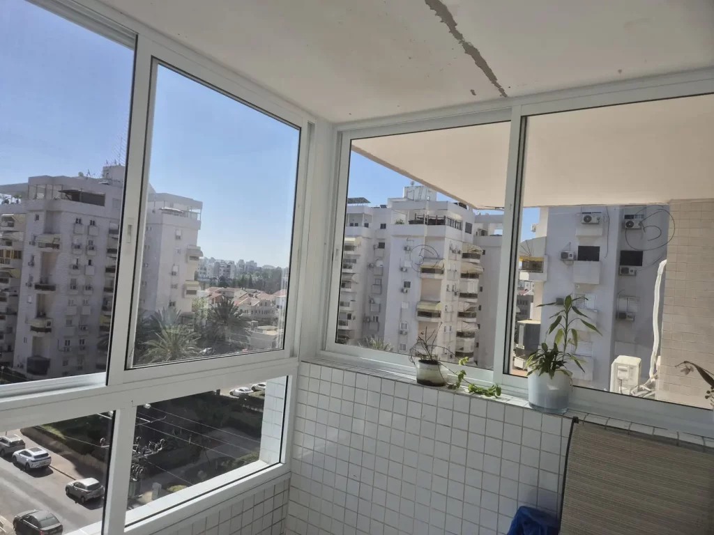 סגירת מרפסת פינתית מאלומיניום לבן עם נוף לבנייני מגורים