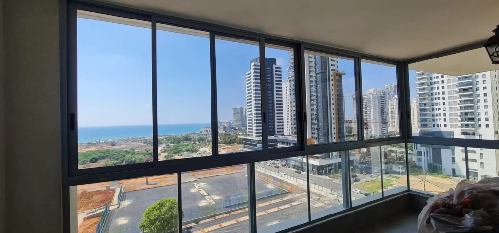 סגירת חורף למרפסת במסגרות אלומיניום שחורות עם נוף לים